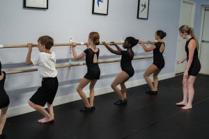 A teacher instructing young students at the barre practising their pliés.